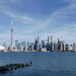 Pohled na Toronto skyline z jezerního břehu Lake Ontario v podzimním dni — běžní cestovatelé pozorují město přes vodu