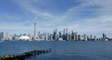 Pohled na Toronto skyline z jezerního břehu Lake Ontario v podzimním dni — běžní cestovatelé pozorují město přes vodu