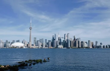 Pohled na Toronto skyline z jezerního břehu Lake Ontario v podzimním dni — běžní cestovatelé pozorují město přes vodu