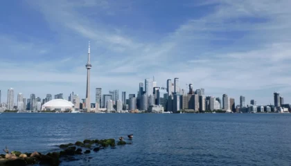 Pohled na Toronto skyline z jezerního břehu Lake Ontario v podzimním dni — běžní cestovatelé pozorují město přes vodu